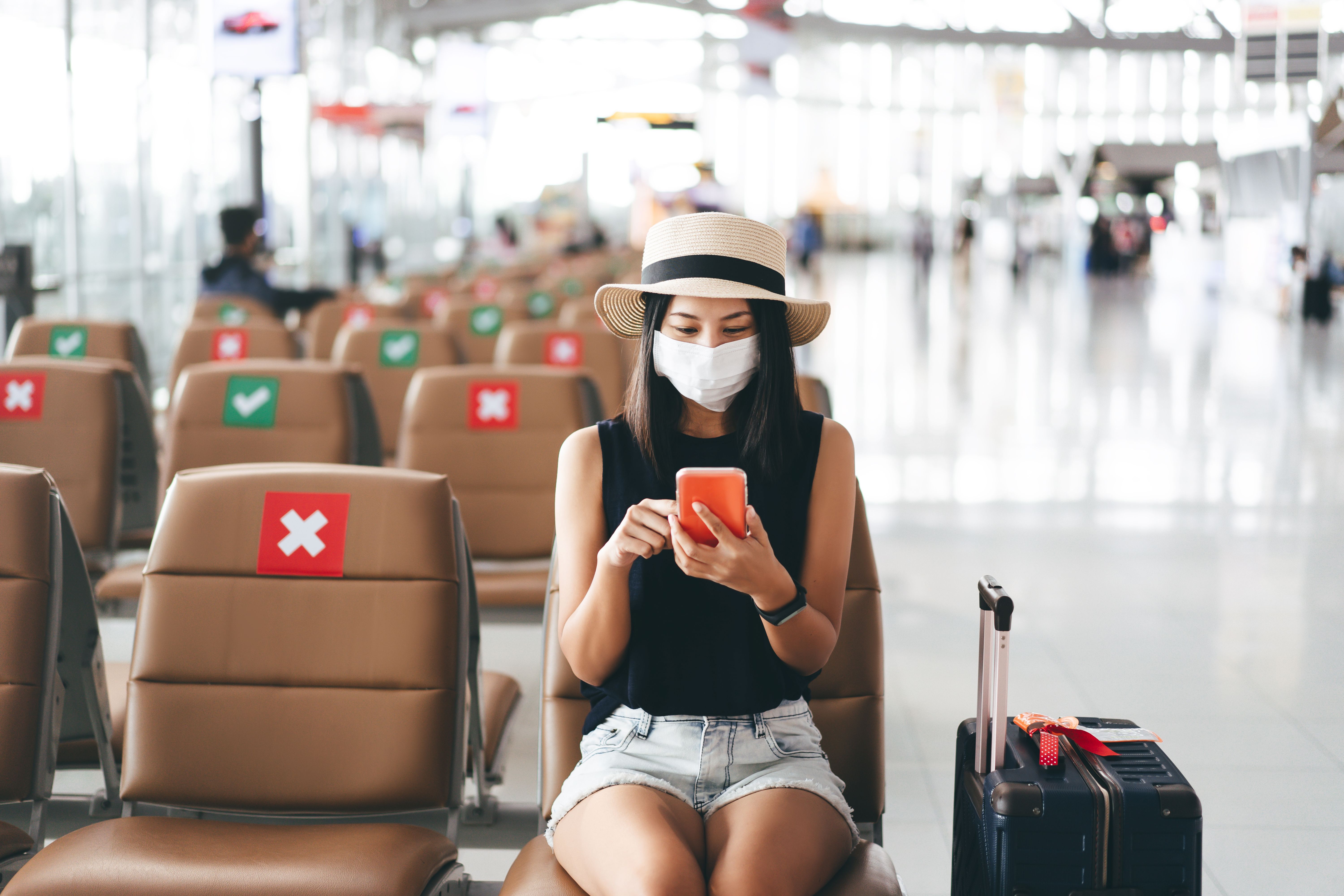 As viagens internacionais agora são restritas e o Departamento de Estado dos EUA está pedindo aos viajantes que 'reconsiderem seriamente' 2 sentado em um aeroporto usando uma máscara facial