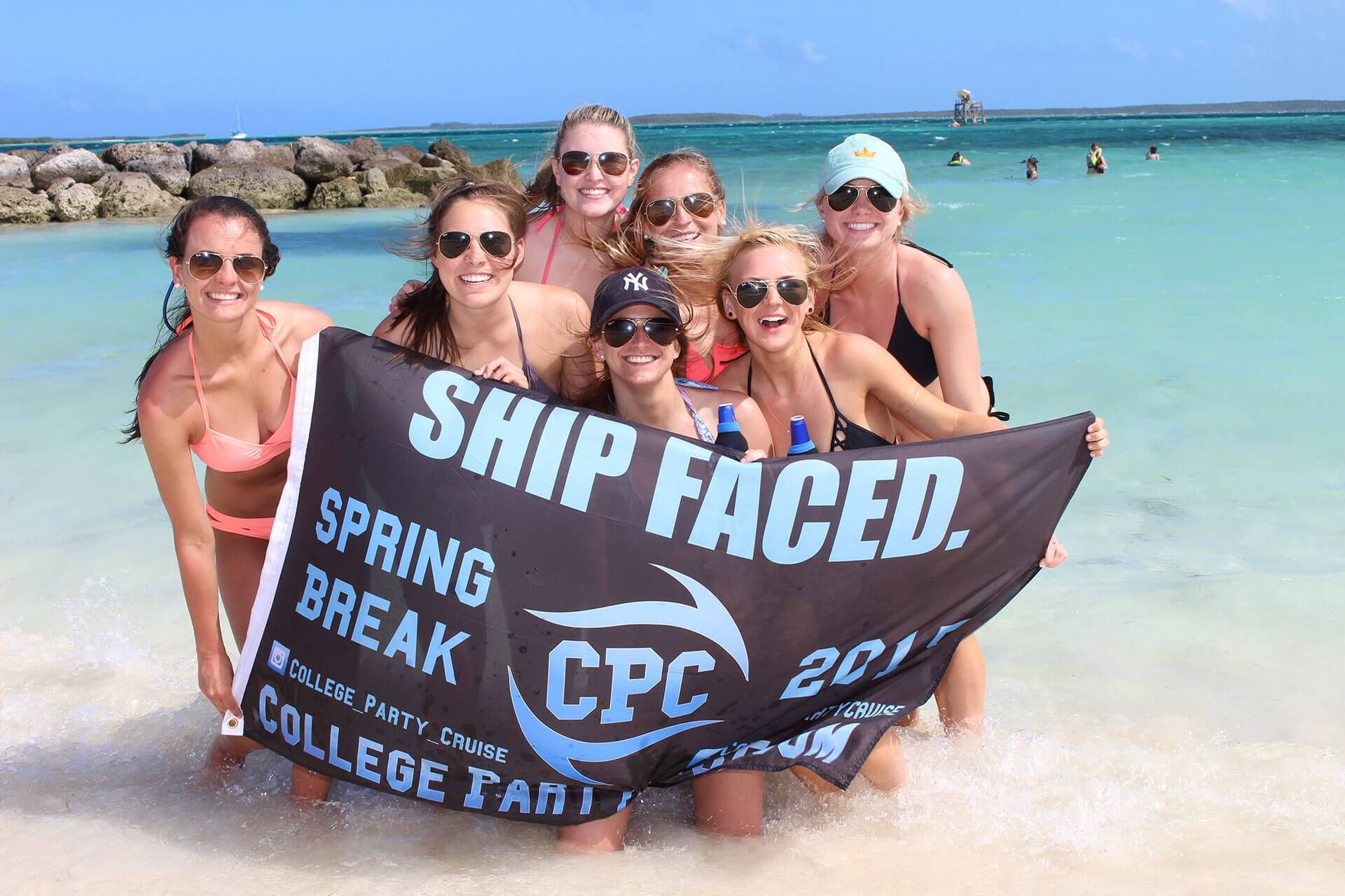 Grupo de estudantes universitários em uma praia segurando uma placa que diz Ship Faced